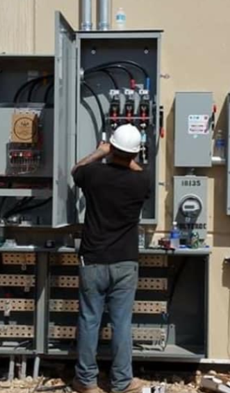 A man in white hard hat standing next to an electrical box.