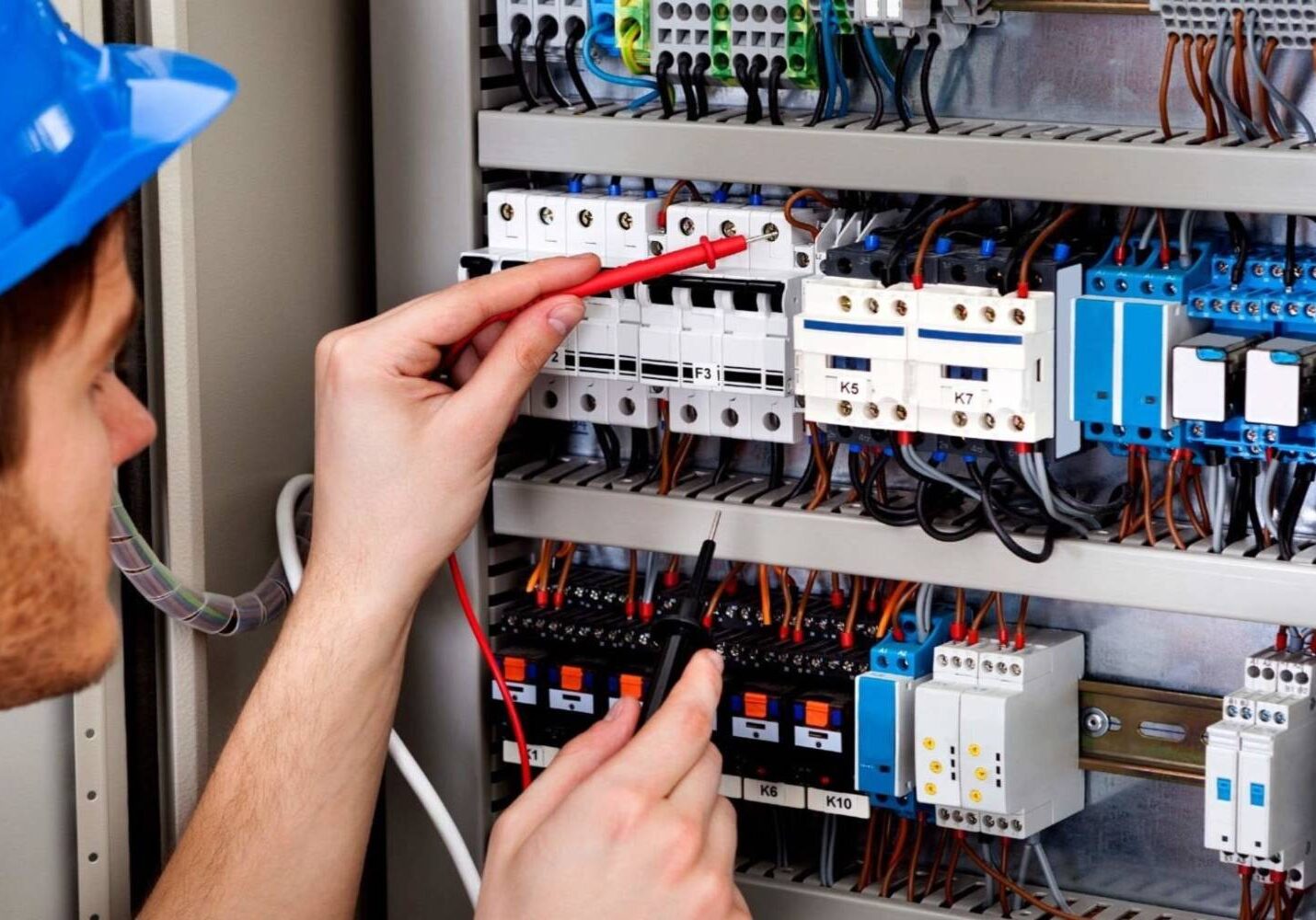 A person is working on electrical equipment in an industrial setting.