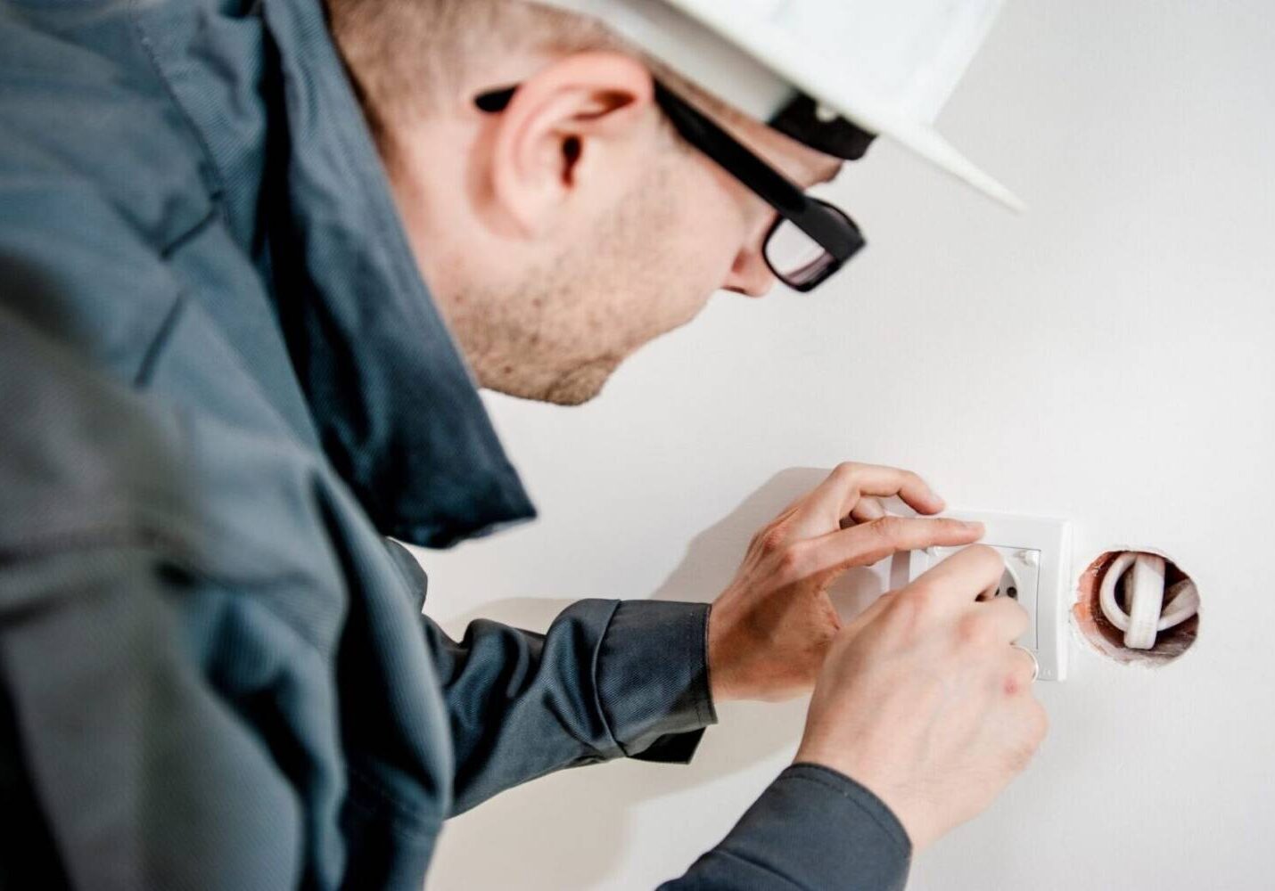 A man in glasses and hard hat working on a wall.